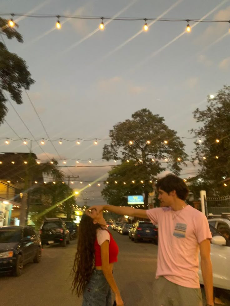 a man and woman walking down the street at dusk with string lights strung above them