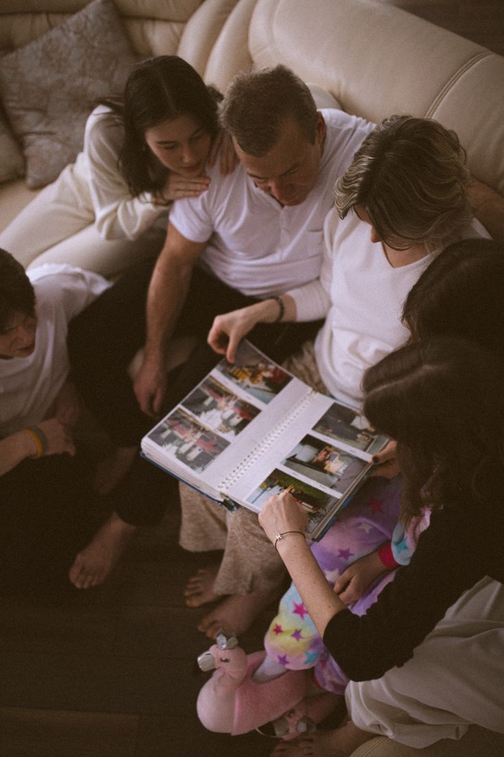 a group of people sitting on top of a couch next to each other holding an open book