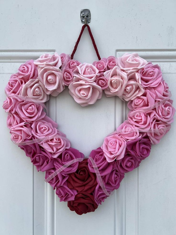 a heart shaped wreath made out of pink and red roses hanging on a white door