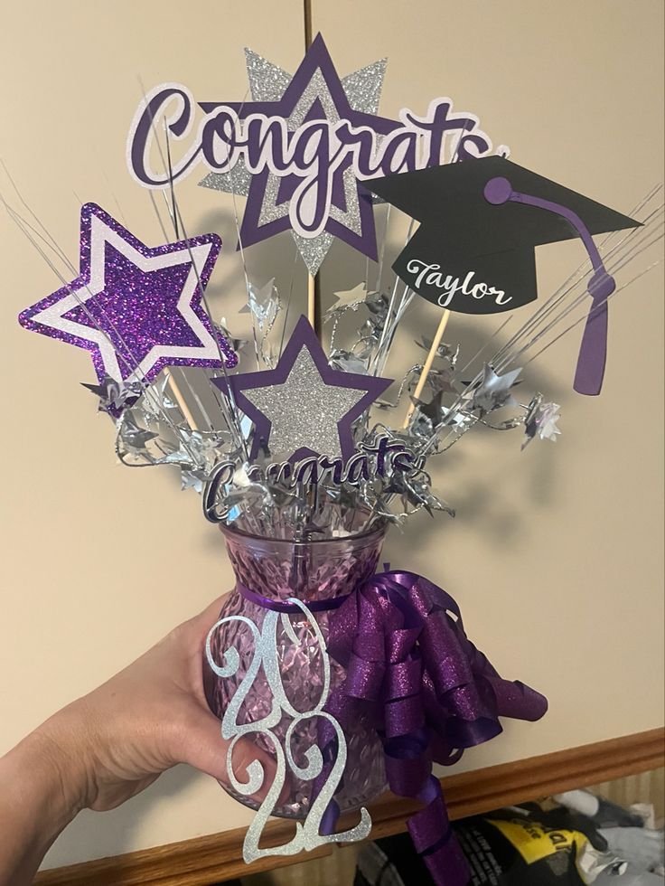 purple and silver graduation centerpieces in a glass vase with star toppers on it