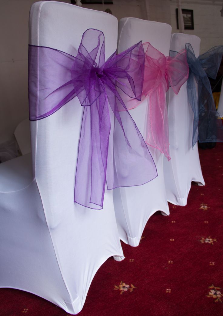 row of white chairs with purple bows on them