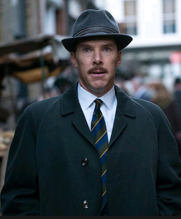 a man wearing a suit and tie with a hat on his head standing in the street