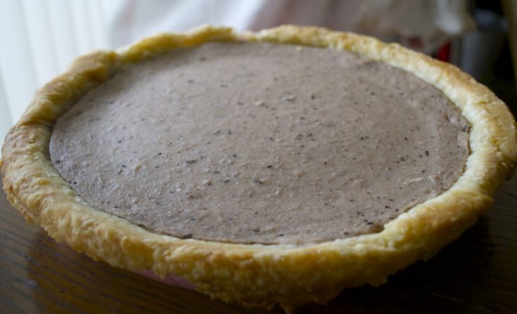 a pie crust on a wooden table with a person in the background looking at it