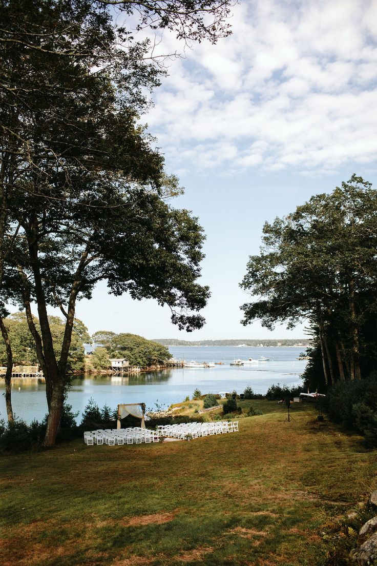 an outdoor wedding setup with white chairs and water in the background, surrounded by trees