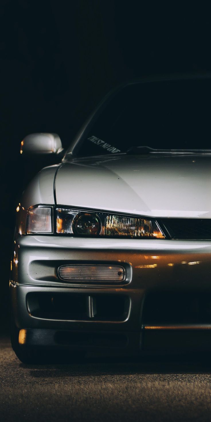 the front end of a silver sports car parked in a dark spot with its lights on