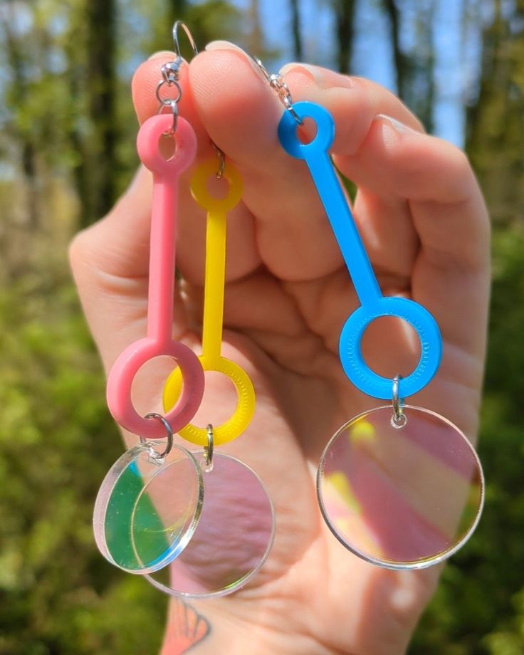 a person holding up three pairs of earrings in their hand with trees in the background