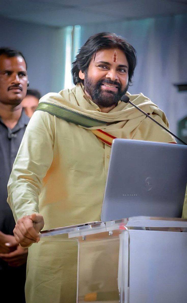 a man standing at a podium with a laptop in front of him and another man behind him