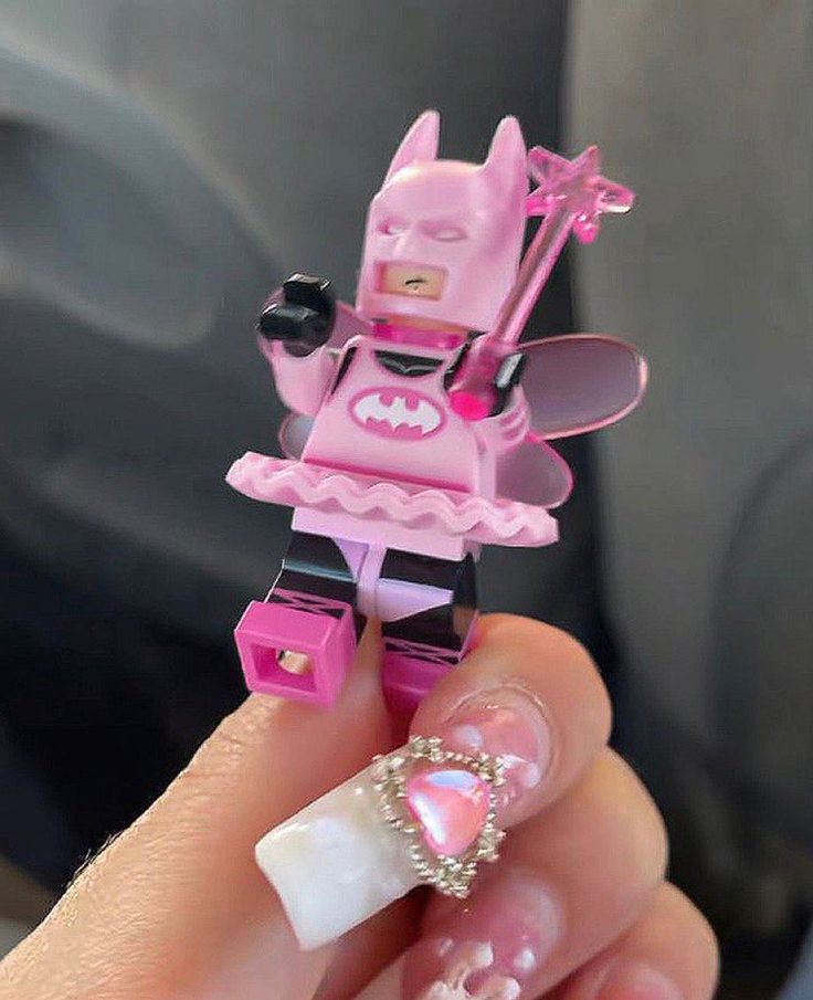 a hand holding a pink lego toy with white nails and an acrylic manicure