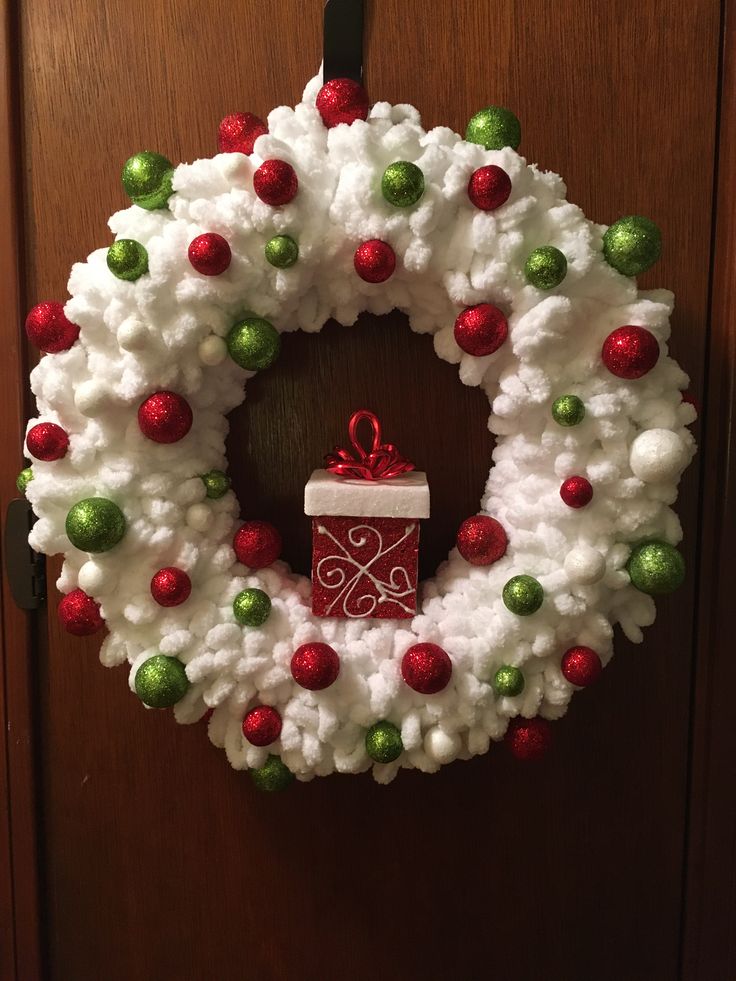 a white wreath with red, green and white ornaments hanging on the front door next to a brown door