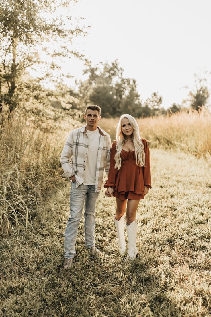 a man and woman are standing in the middle of an open field with tall grass