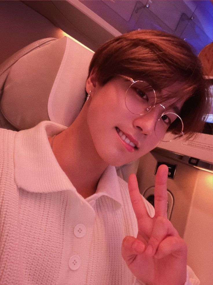 a young man in glasses making the peace sign with his hand while sitting on an airplane