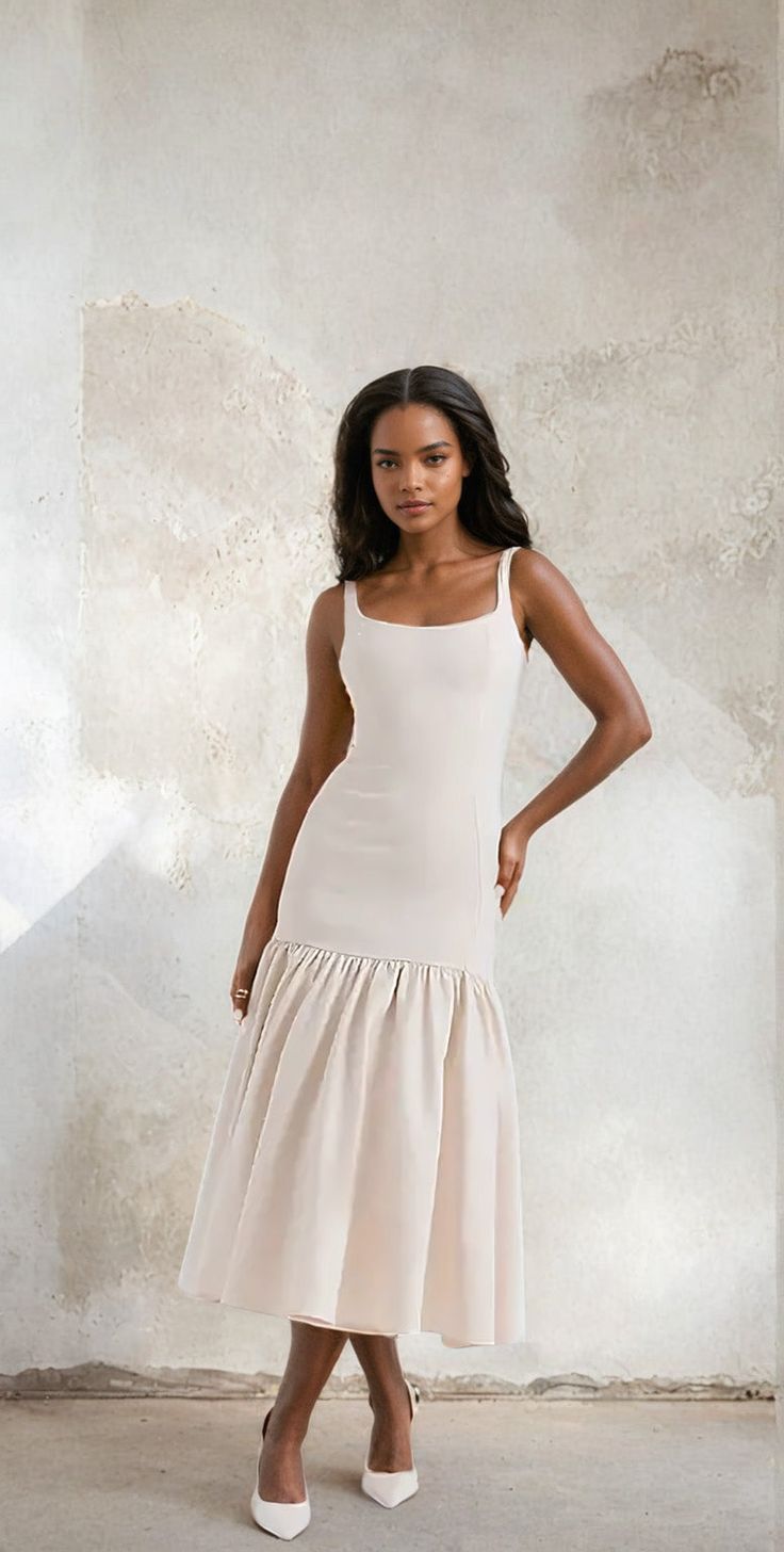 a woman standing in front of a wall wearing a white dress and heels with her hands on her hips