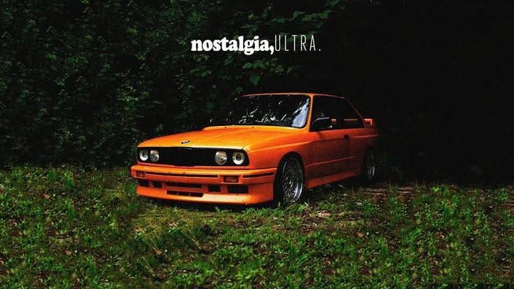 an orange car is parked in the grass near some trees and bushes at night time