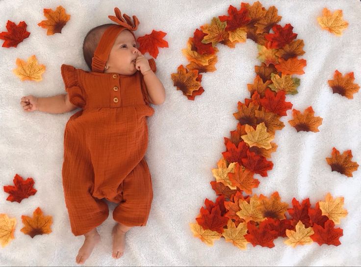 a baby laying on top of a blanket covered in leaves next to the letter s