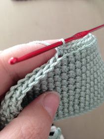 a hand holding a red crochet hook in front of a green knitted object