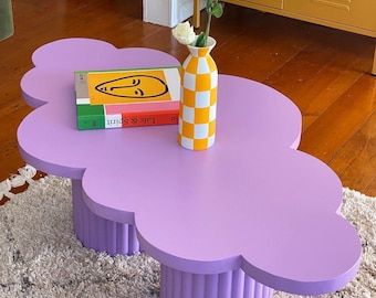 a purple table with a flower in a vase and books on the top is shown