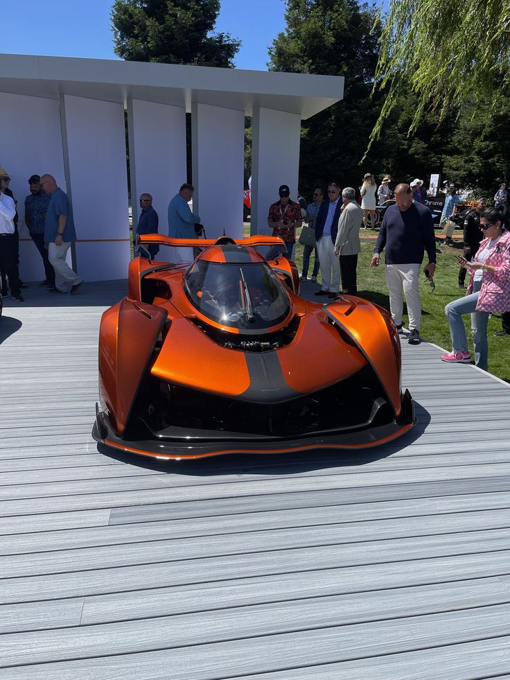 an orange race car parked on top of a wooden platform next to people standing around