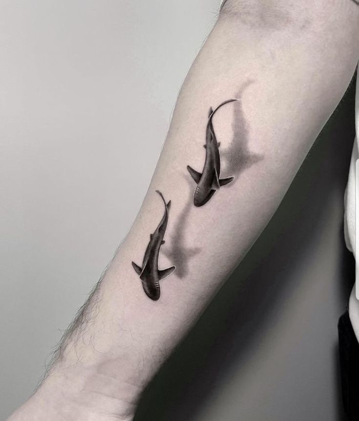 three shark tattoos on the left forearm and arm are shown in black ink, while one is