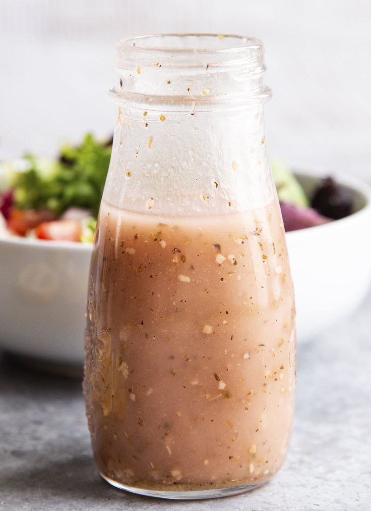 a glass jar filled with dressing next to a bowl of salad