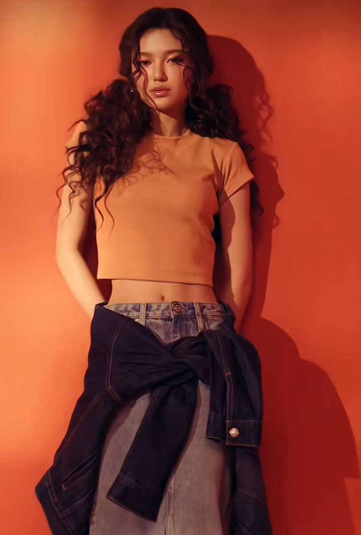 a woman standing in front of an orange wall with her hands on her hips wearing a skirt