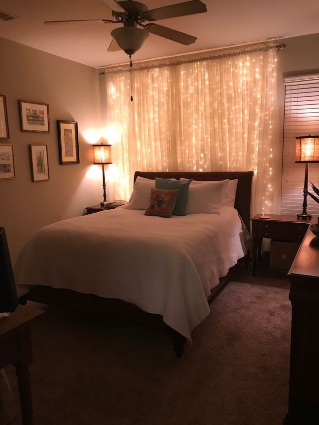 a bed sitting in a bedroom next to a window covered in white curtains and lights