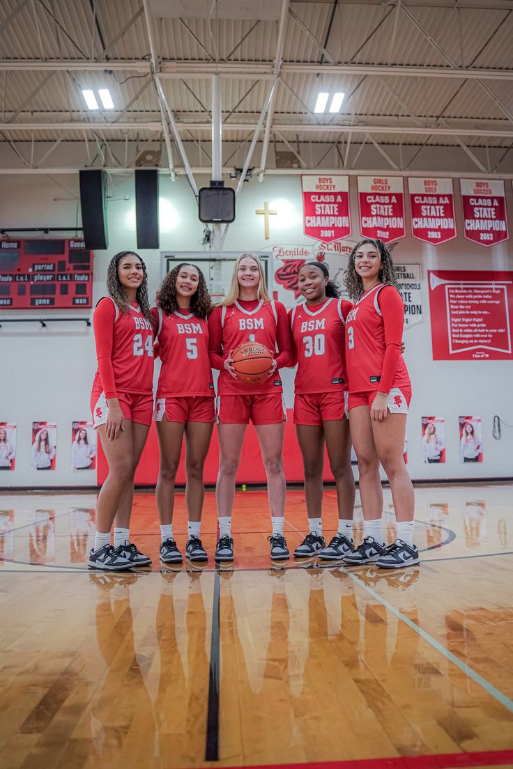 a group of girls in red uniforms standing on a basketball court with their arms around each other