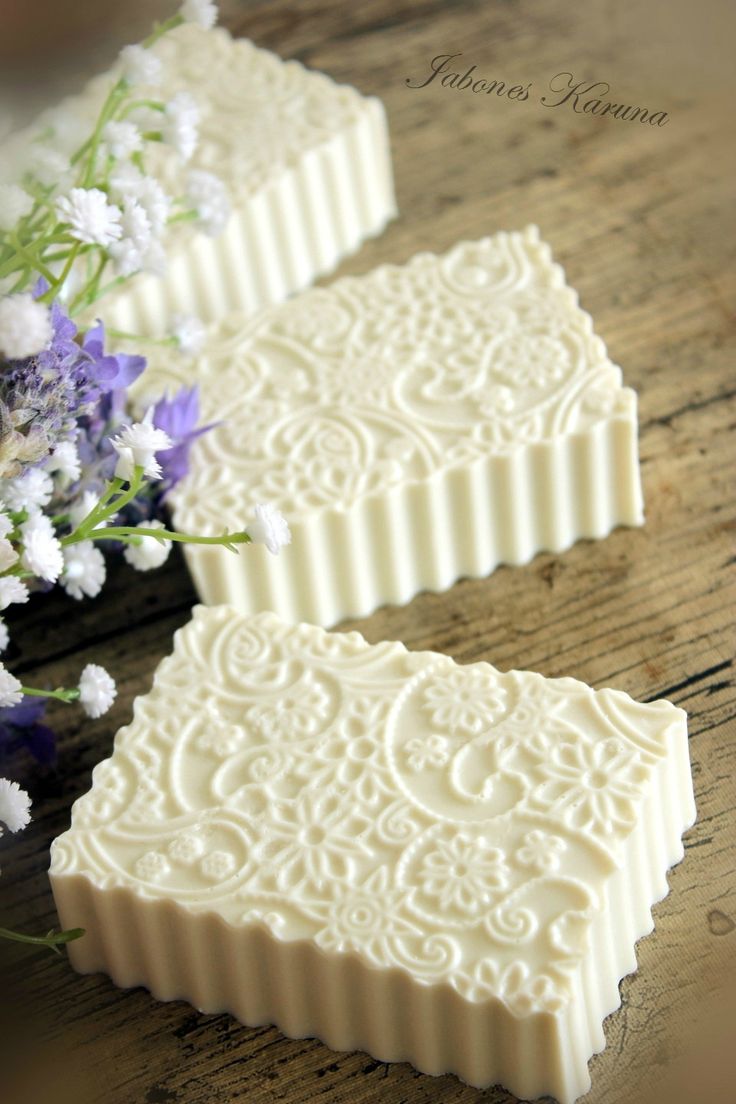 two white soap bars sitting on top of a wooden table next to purple and white flowers