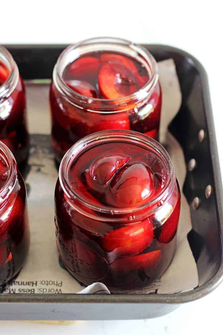 four jars filled with red fruit sitting on top of a metal tray next to each other