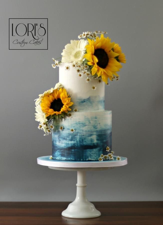 a three tiered cake with sunflowers on the top and blue icing