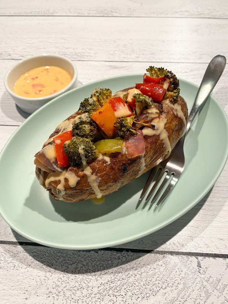 baked veggie loaded baked potato on a plate with a fork and bowl of soup