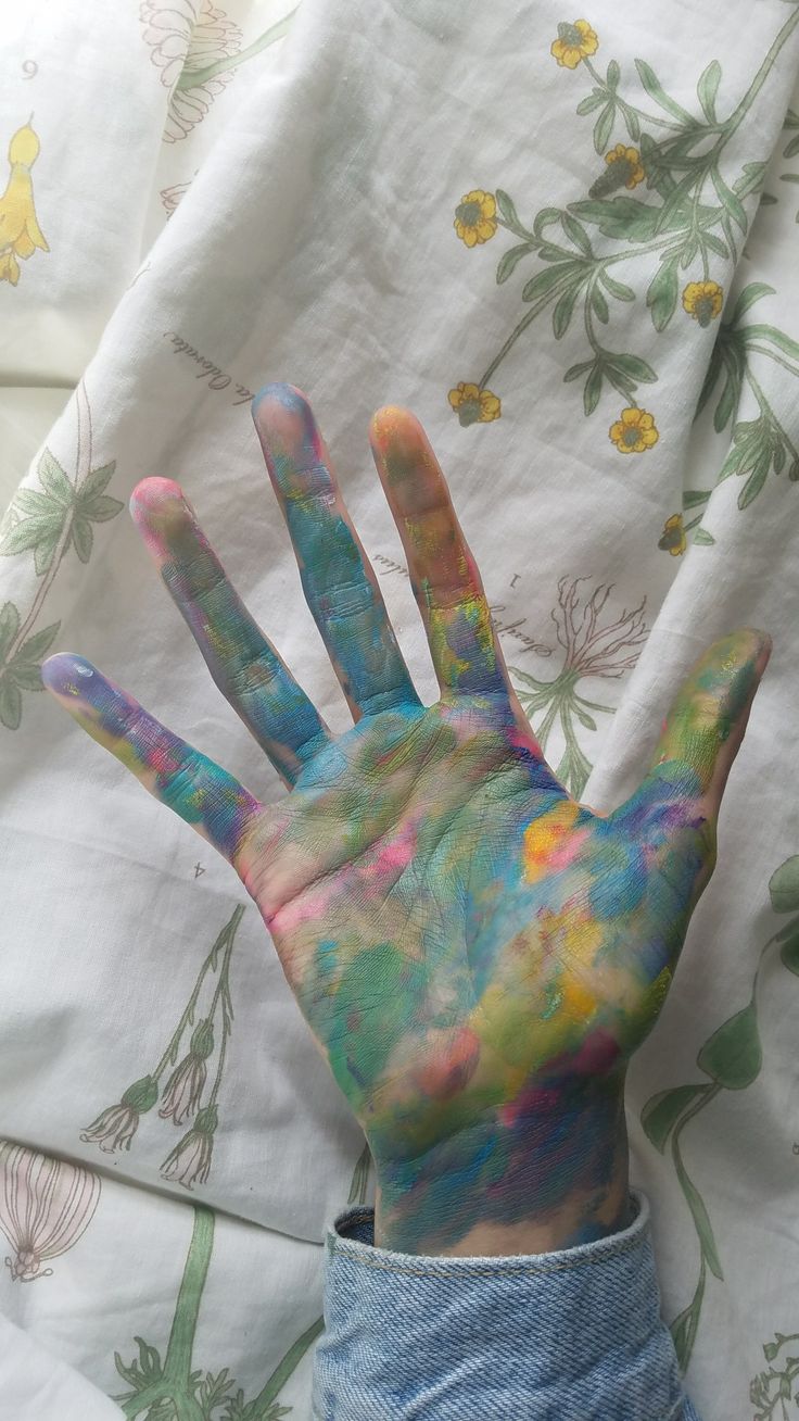 a person's hand covered in multicolored paint sitting on top of a bed