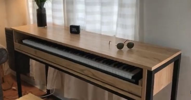 a piano sitting in front of a window next to a vase with flowers on it