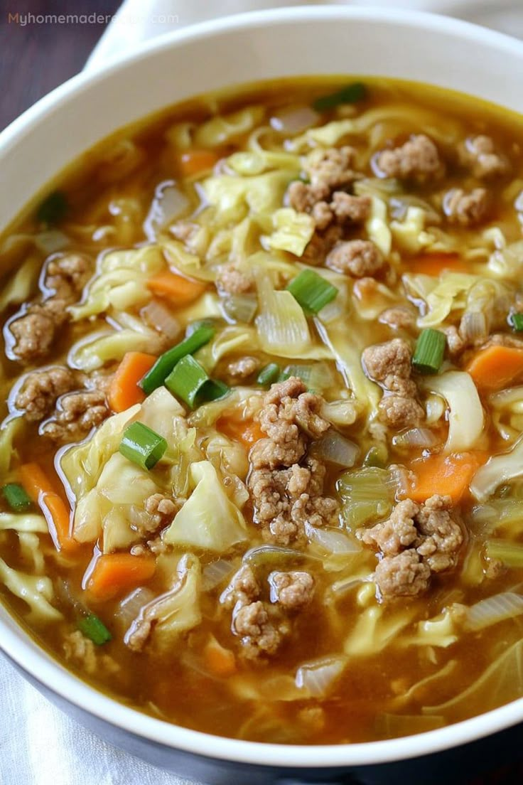 a white bowl filled with meat and cabbage soup on top of a wooden table next to a napkin