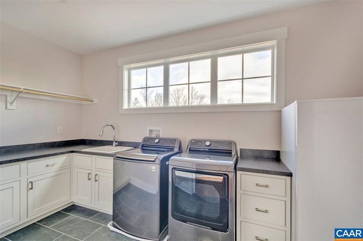 an empty kitchen with white cabinets and stainless steel appliances in the center, along with two washers and dryer combos