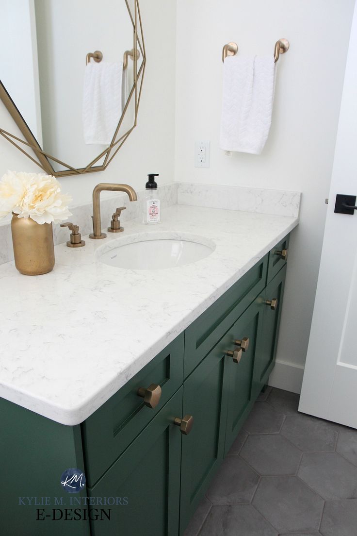 a bathroom with green cabinets and white counter tops, gold accents on the faucet