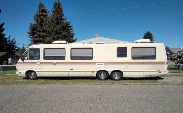 an rv parked on the side of the road in front of a fence and trees