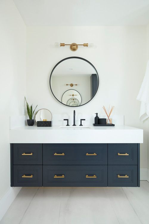 a bathroom vanity with two sinks and a large round mirror above it, in front of a white wall