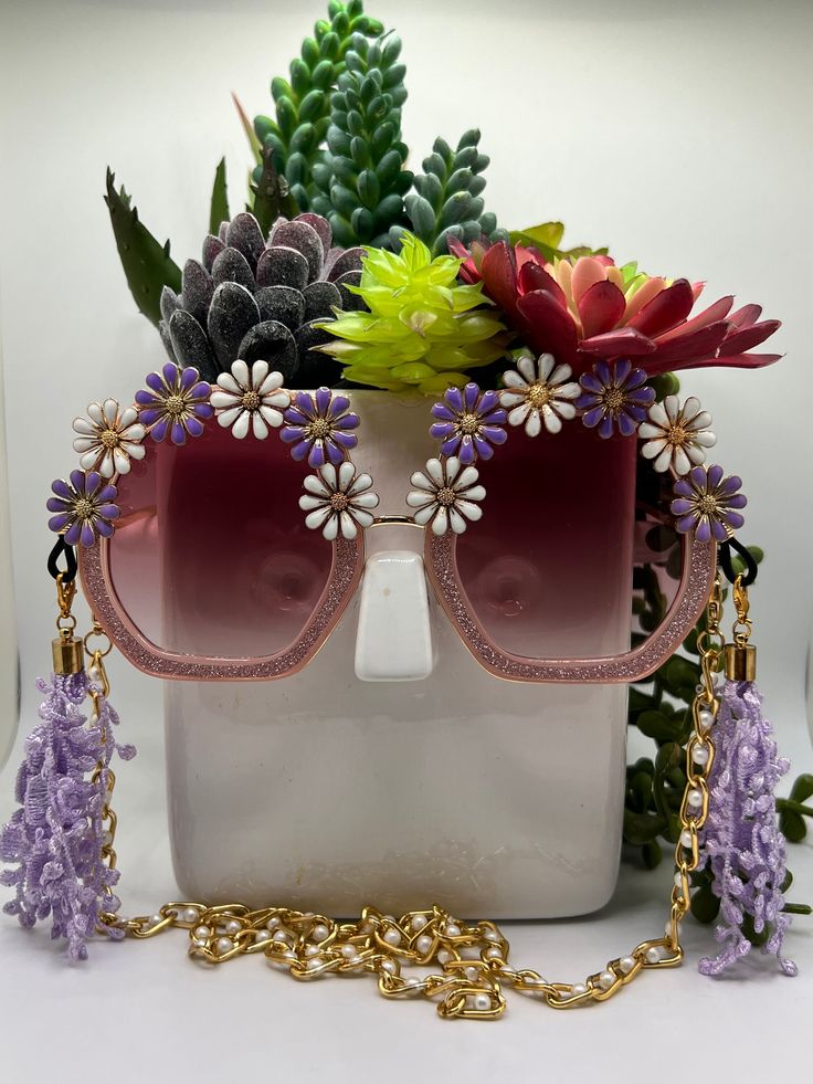 Daisies surround these polygon, square glittering sunglasses and are accompanied by an adjustable and removable eyewear chain and removable tassels. Featuring bold, fashion-forward designs, these glamorous sunglasses are perfect for making an entrance at any special occasion. Embellished and colorful, these fun and inspiring sunglasses will make sure you stand out in a crowd. Ideal for bachelorette parties, Vegas trips, weddings, birthdays, and more - Roaring Sunnies are the perfect accessory to Purple Party Sunglasses, Summer Party Glasses Chains, Gold Party Sunglasses With Adjustable Fit, Purple Plastic Party Sunglasses, Party Sunglasses With Purple Gradient Lenses, Party Purple Sunglasses With Gradient Lenses, Purple Sunglasses With Gradient Lenses For Party, Multicolor Glasses Chains For Summer Parties, Multicolor Summer Party Glasses Chain