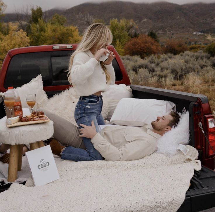 a man and woman laying in the bed of a pickup truck with food on it