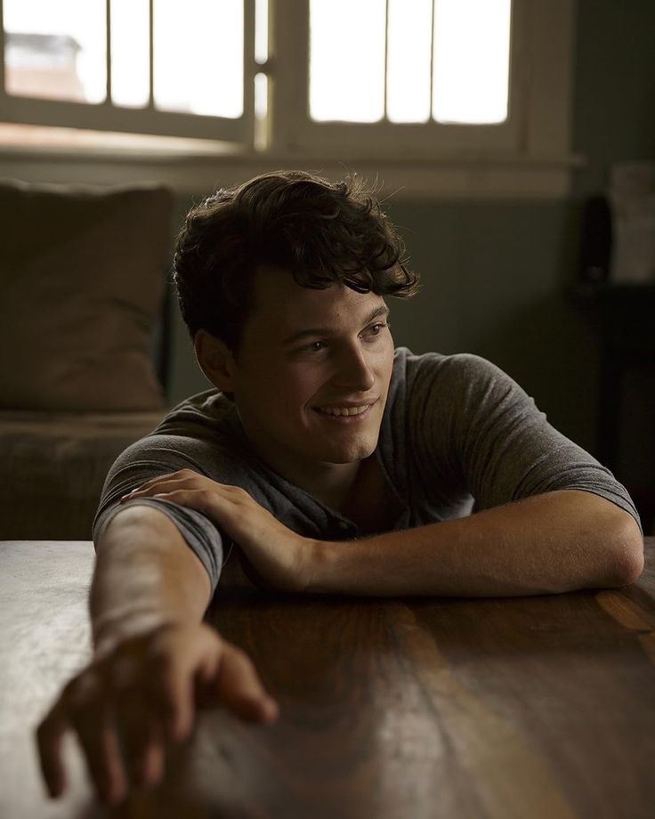 a young man sitting at a table with his arms crossed and looking off to the side