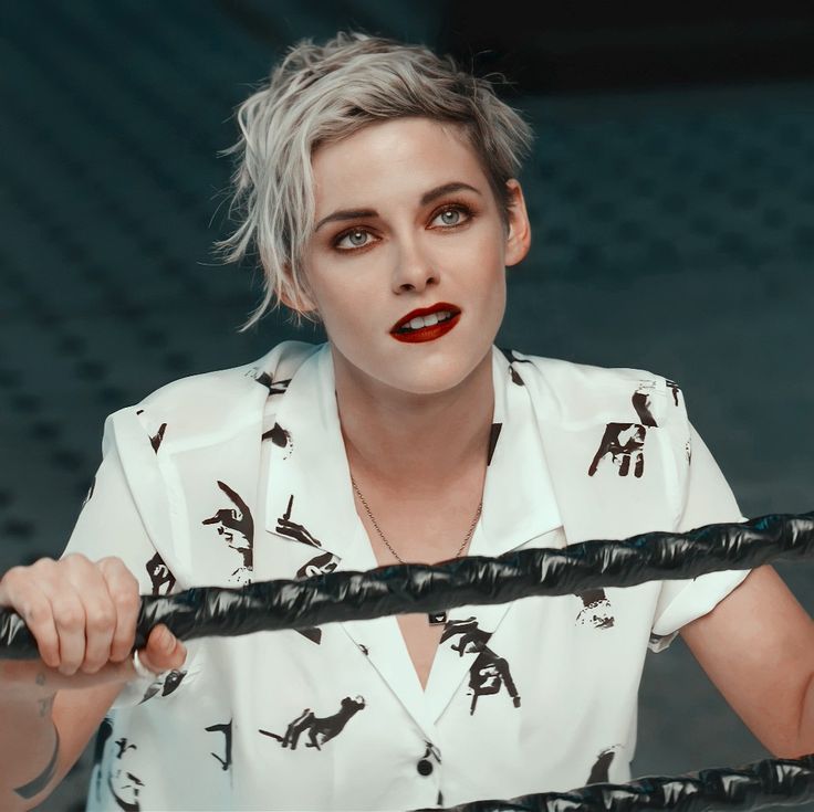 a woman with grey hair holding onto a black rope and looking at the camera while wearing a white shirt