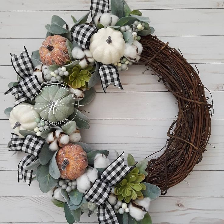 a wreath with pumpkins, cotton and greenery on a white wooden wall background