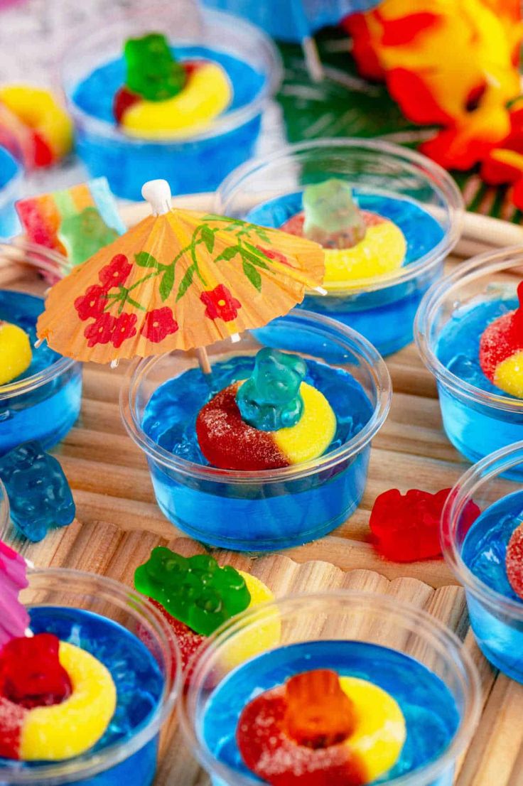 colorful gummy bears in plastic cups on a bamboo tray with an umbrella over them