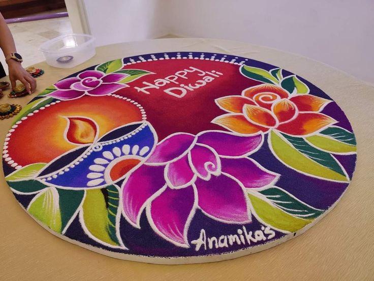 a colorful cake with flowers on it sitting on a table next to a woman's hand