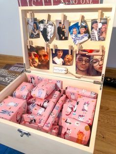 a wooden box filled with lots of pink wrapped gift boxes and pictures hanging on clothes pins