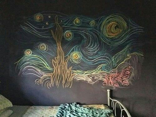 a bed with a blanket on top of it next to a chalkboard wall painting