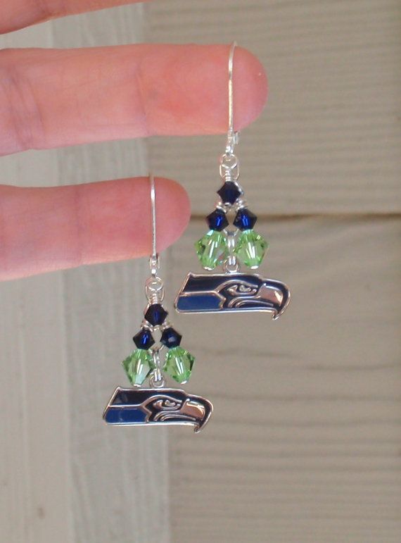 a pair of seattle football earrings with swarong crystals and beads is being held by someone's hand