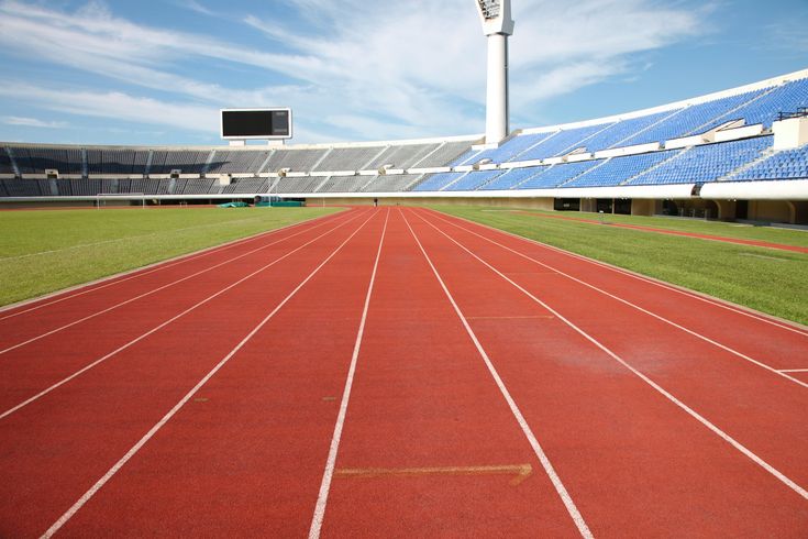 an empty running track in a stadium with blue sky and white clouds above the stands