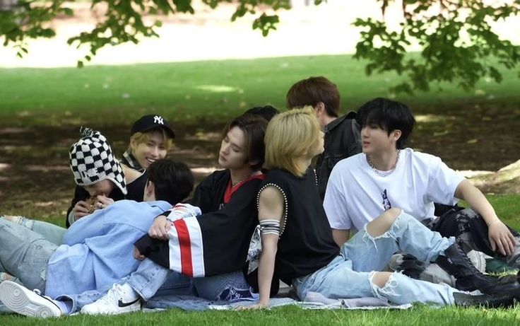 group of young people sitting on the grass in front of a tree with their backs to each other