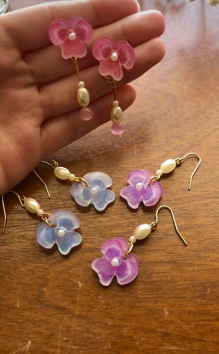 four flower shaped earrings are being held by someone's hand on a wooden table